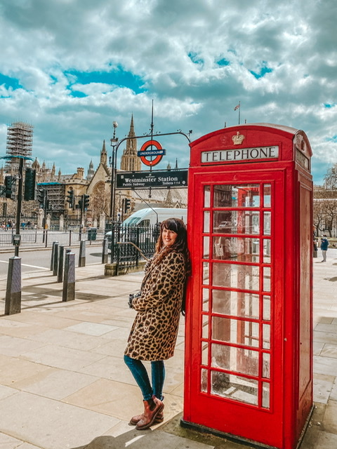 London phone box outside the House of Parliament. Woman leaning on box with Westminster station behind 
